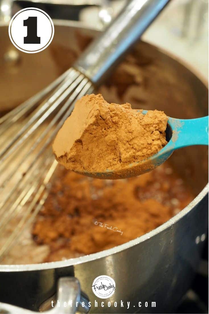 heaping blue tablespoon with cocoa powder over a pot with melted butter and a whisk