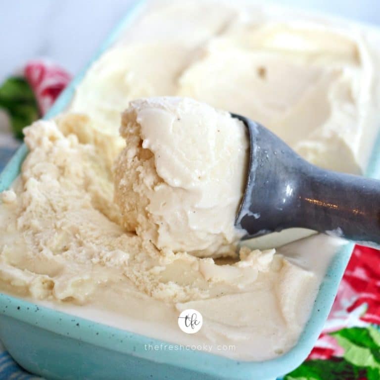 Square image of homemade old fashioned ice cream with vanilla beans with ice cream scoop in a pretty turquoise container.