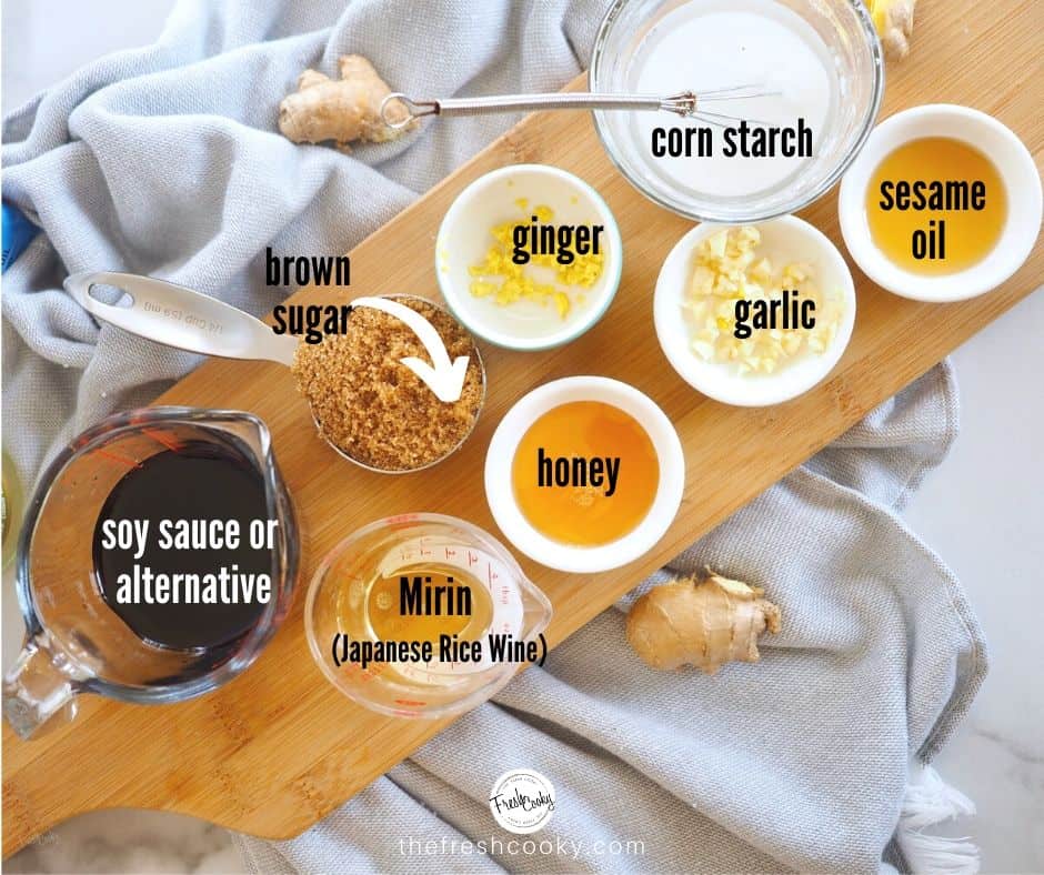 Teriyaki sauce and marinade ingredients in small glass containers laid out on wooden cutting board. Soy sauce, brown sugar, ginger, corn starch, sesame oil, garlic, honey and Mirin.