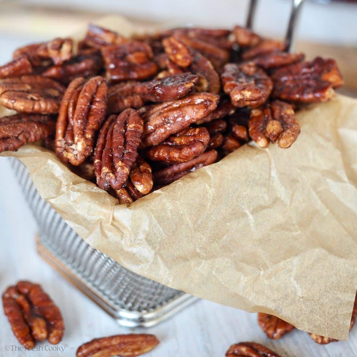 A basket lined with parchment paper and filled with dark roasted maple bourbon pecans.