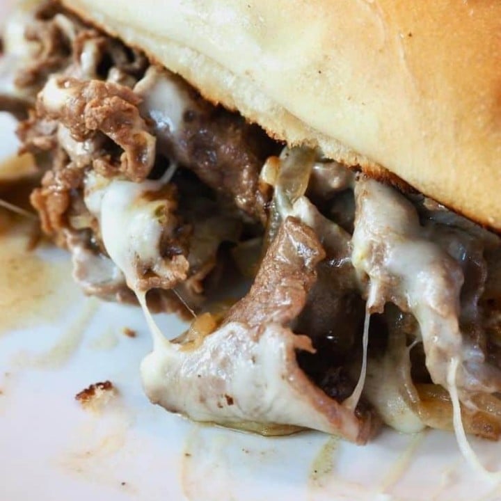 cheesesteak sandwich oozing tender, thinly sliced beef, stringy cheese, juices and caramelized onions with a toasted sub roll