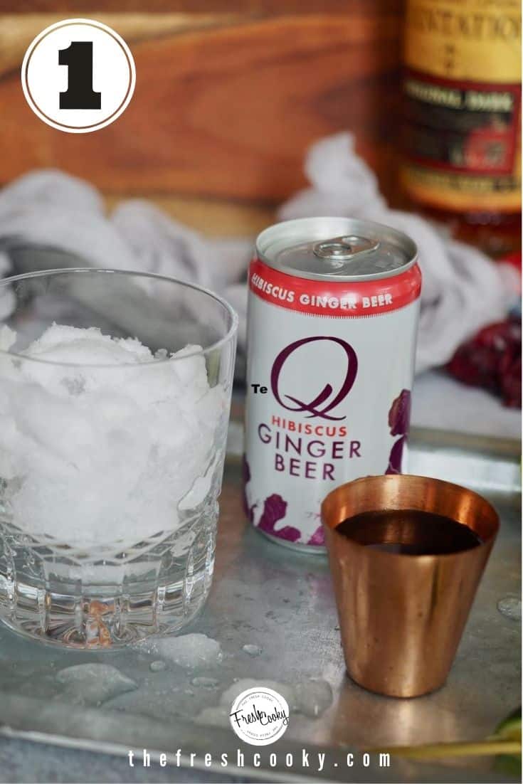 galvanized tray with glass filled with ice, can of hibiscus ginger beer, copper shot glass filled with rum and bottle of dark rum in background.