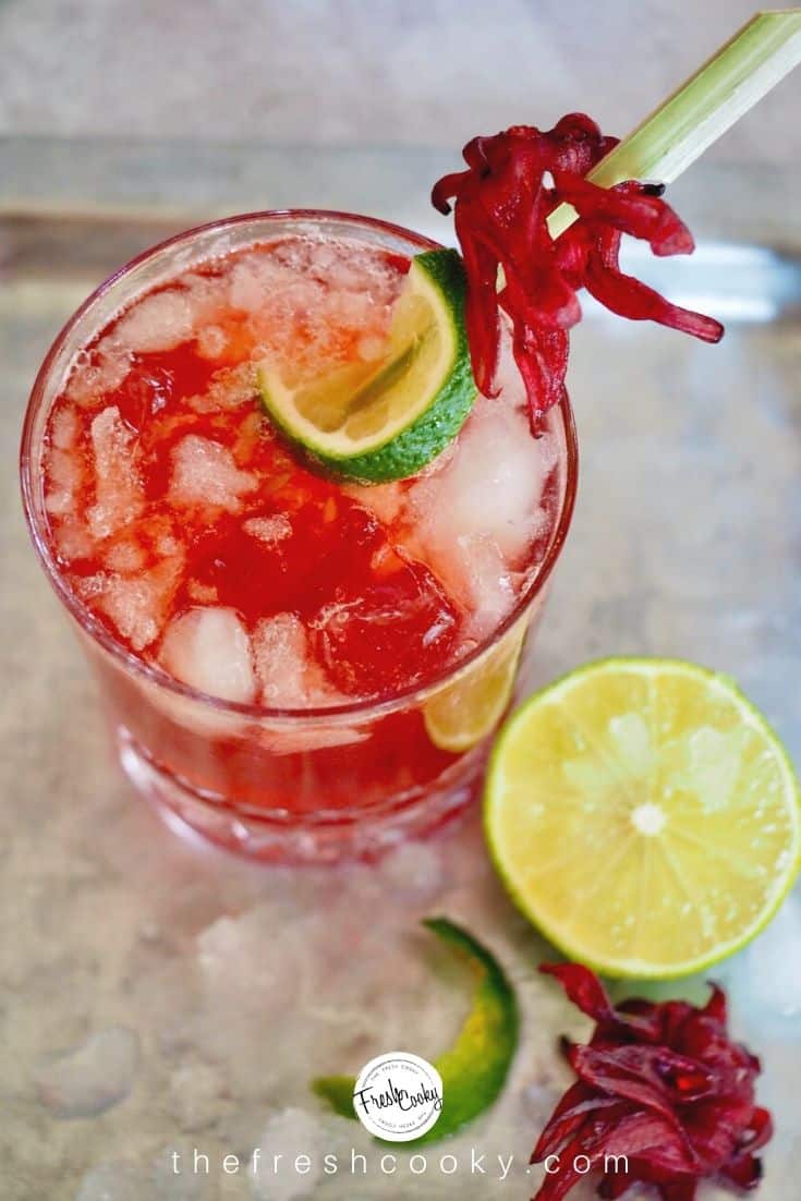 Top down shot of glass with hibiscus ginger beer, rum and lime with a half a lime and hibiscus flower.