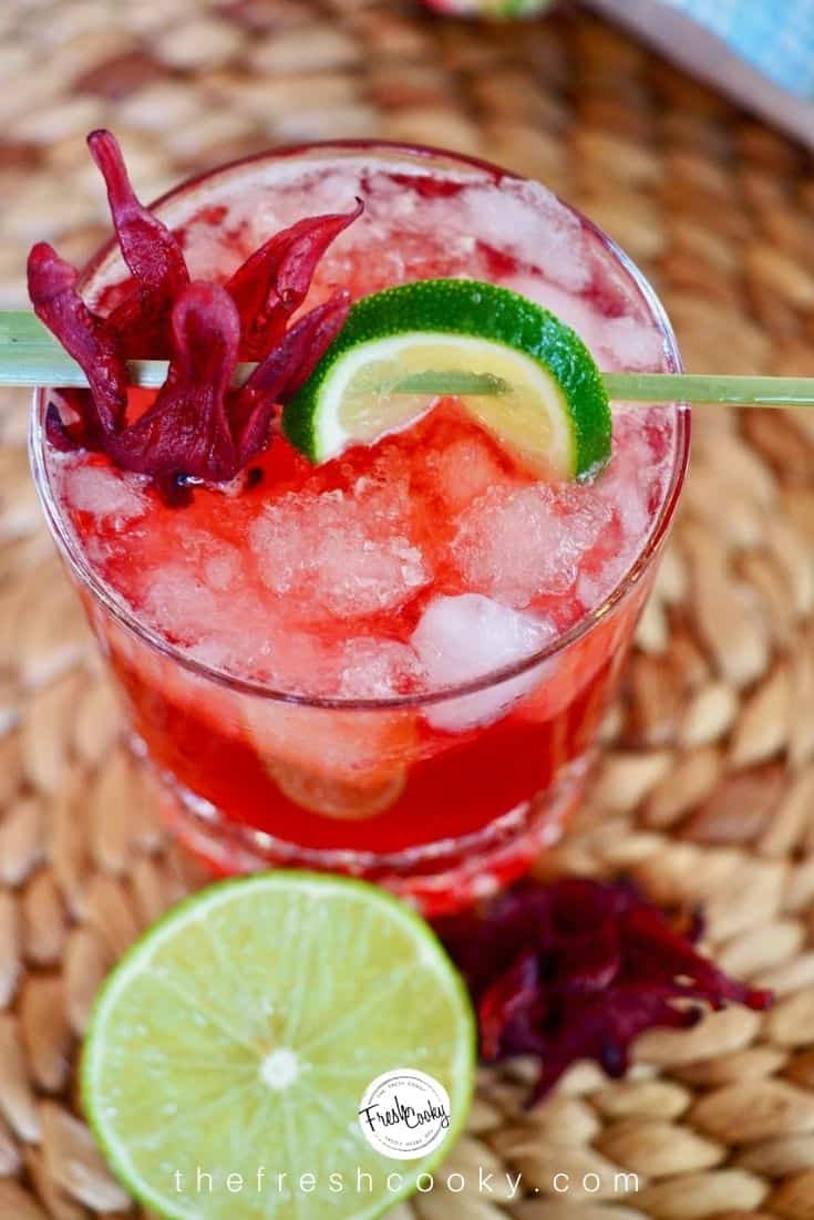 Top down shot of dark and stormy cocktail on rattan mat cocktail garnished with lime, hibiscus flower.