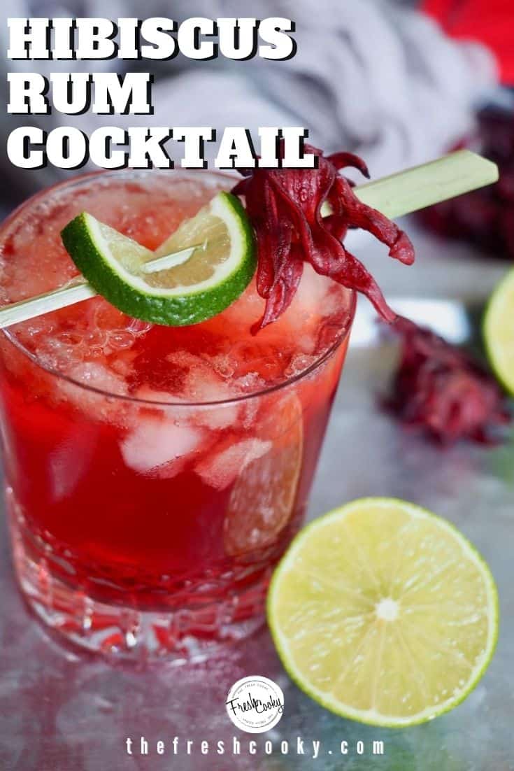 Pinterest image of closeup shot of Dark and Stormy cocktail on platter garnished with slice of lime and dried hibiscus flower, half of lime leaning against the glass.