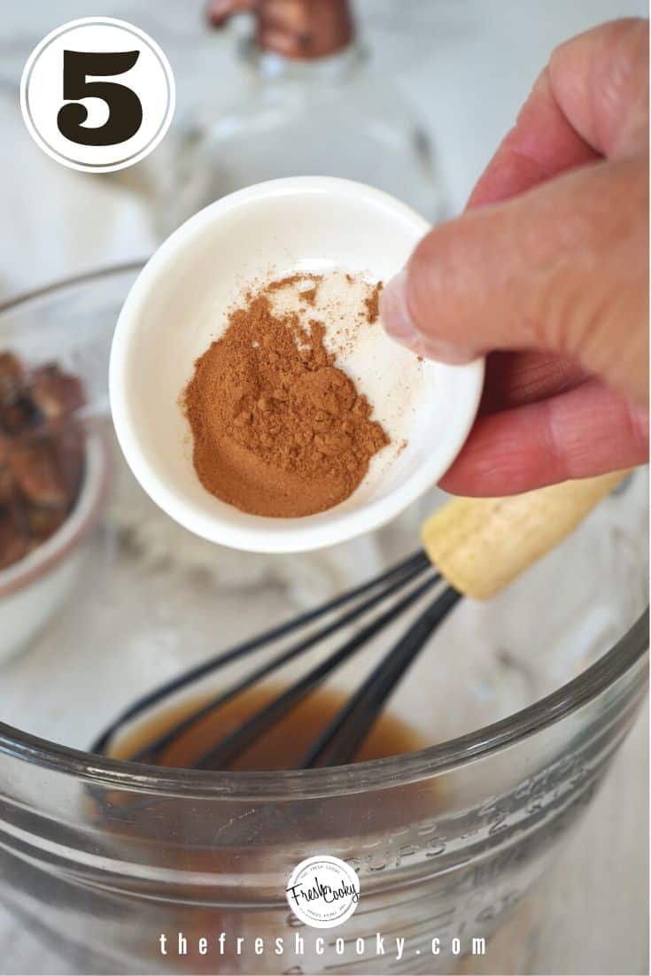 small white bowl with ground cinnamon poured into glass mixing bowl with whisk 