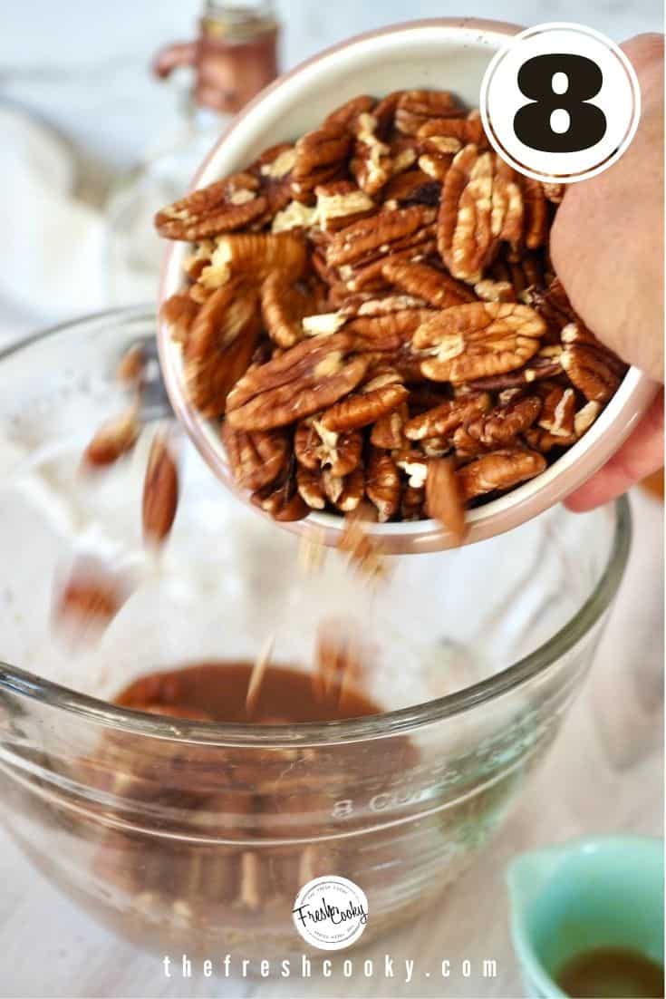 Pouring raw pecans into glass mixing bowl on top of liquid maple bourbon and spice mixture. 