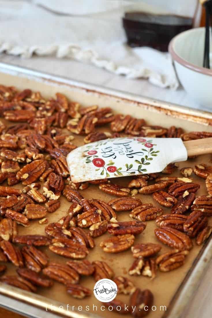 spreading wet pecans in even layer using spatula on parchment lined baking sheet.