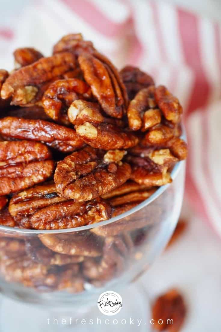 close up shot of maple bourbon candied pecans in glass bowl with red and white striped tea towel in background