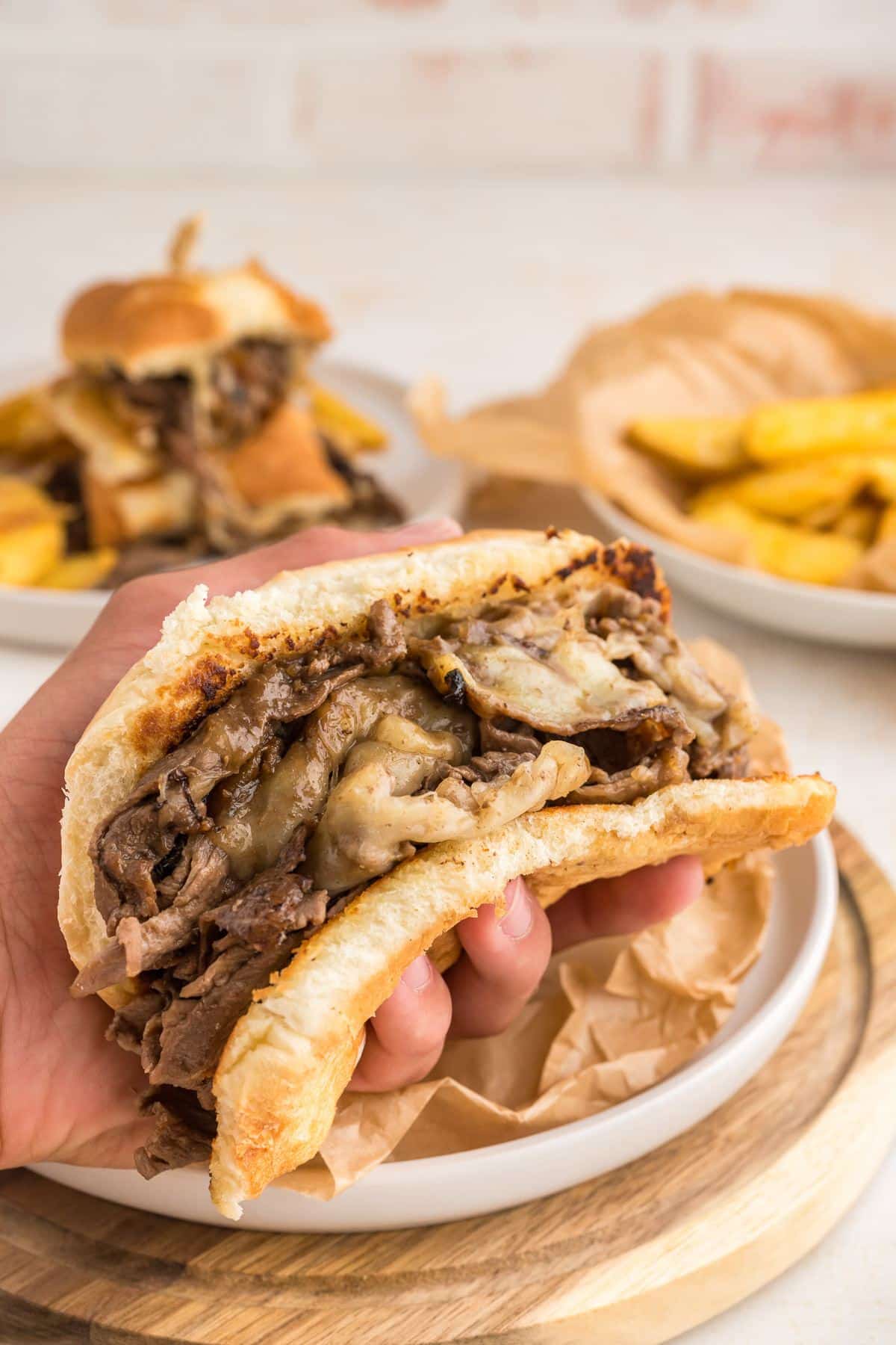 Shaved steak sandwich in had with french fries behind.