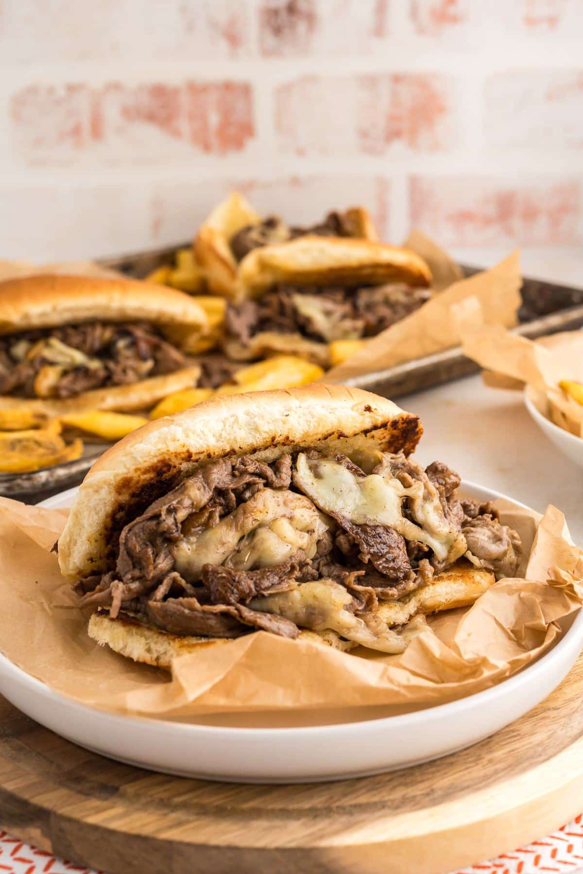 Philly Cheesesteak on a plate with two more sandwiches in the background with steak fries.