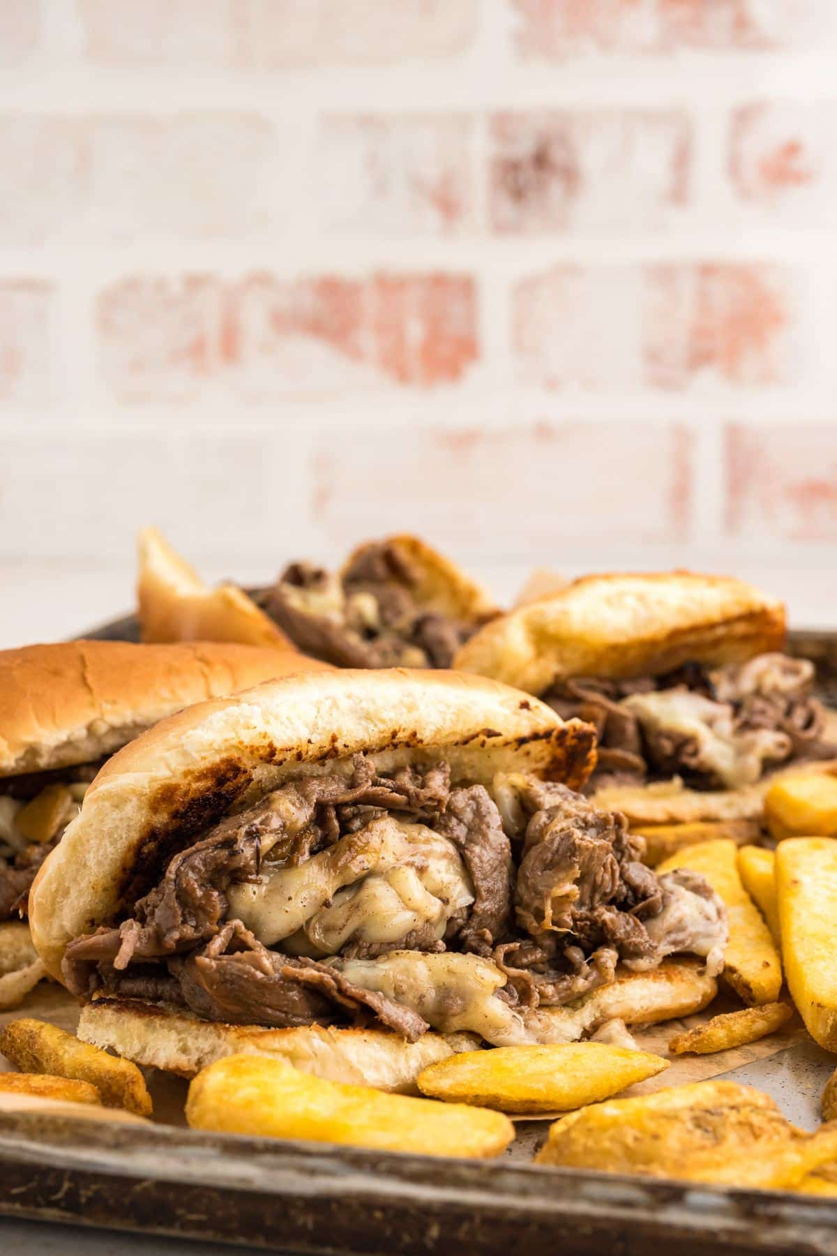 Shaved steak sandwiches on plates with french fries.