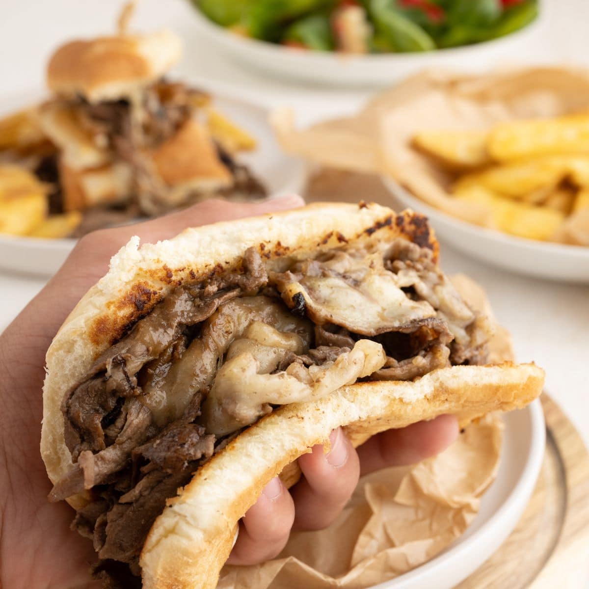 Philly Cheesesteak sandwich held in hand with gooey cheese. Steak and cheese sandwich.