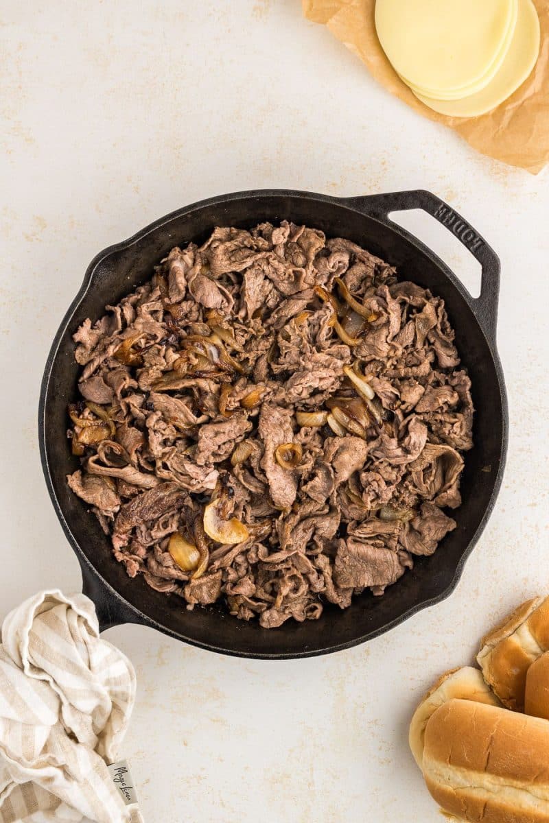 Cast iron skillet with shaved steak and onions mixed in.