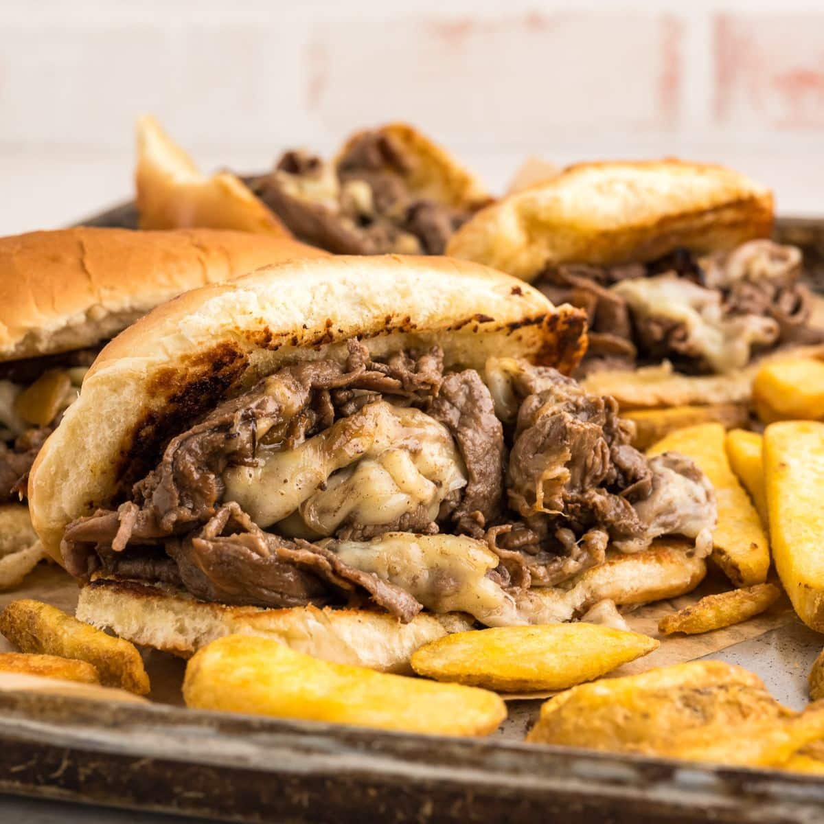 Philly cheese steak sandwich on a tray with french fries surrounding it.