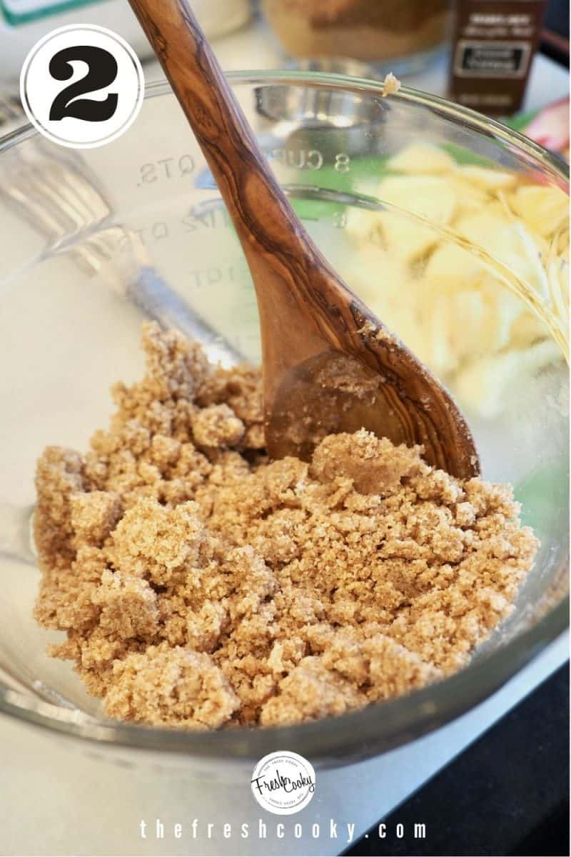 Crumb mixture mixed and sticking into large crumbs with wooden spoon in glass mixing bowl