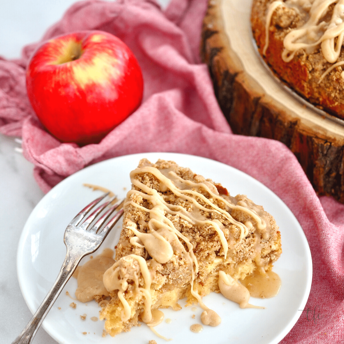 Wedge of Apple Double Crumb Coffee cake on plate with fork, apple behind.