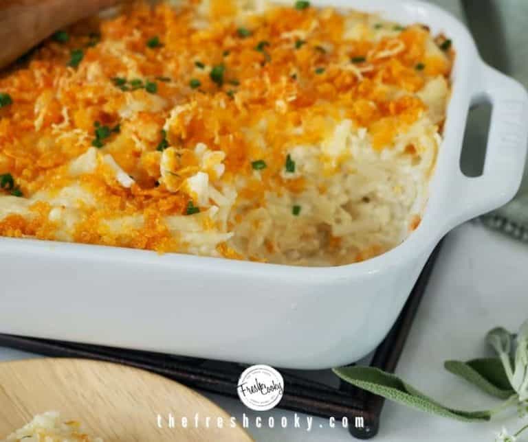 Recipe image of white baking dish filled with cheesy funeral potatoes with a scoop removed.