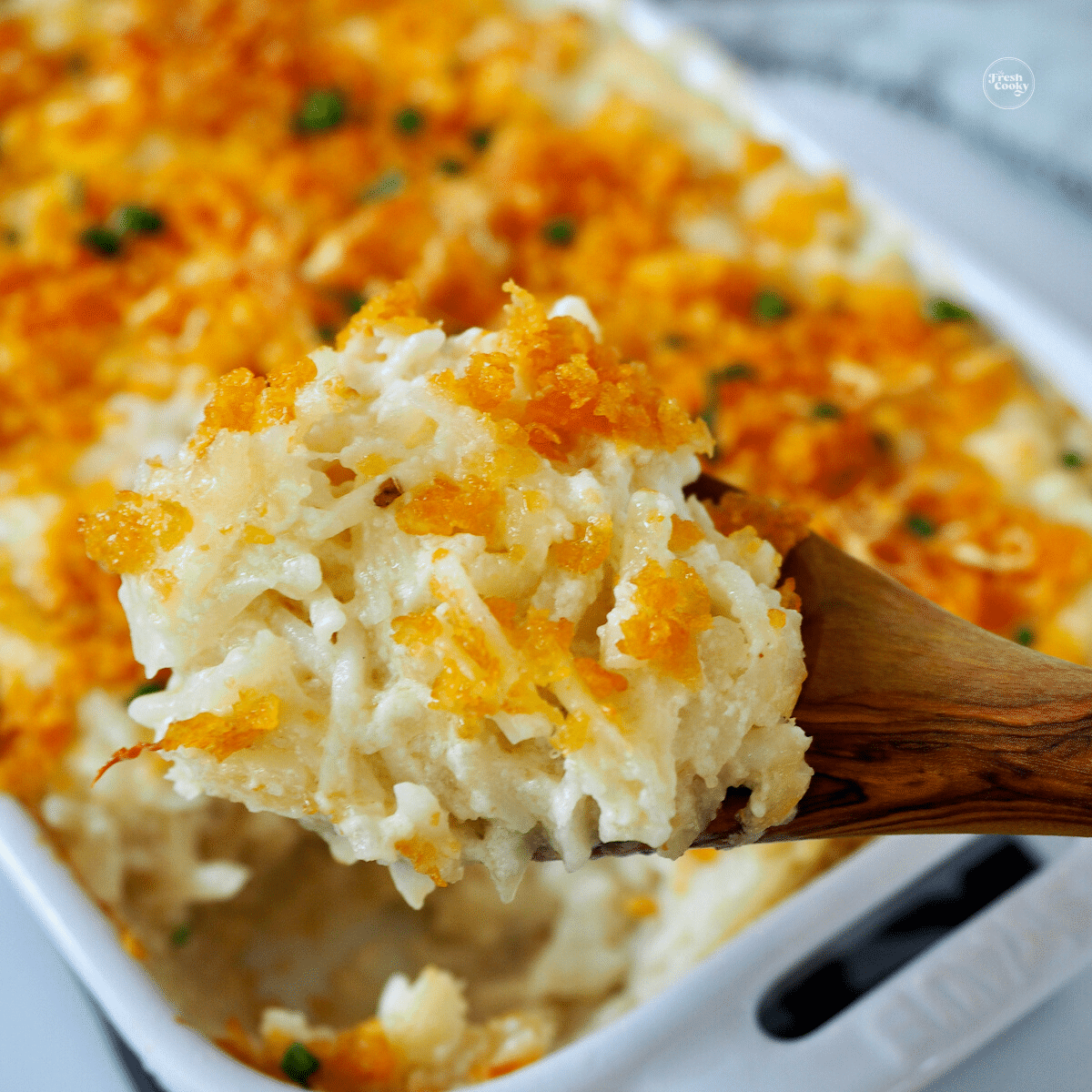 Cheesy Party Potatoes in casserole dish with wooden spoon. 