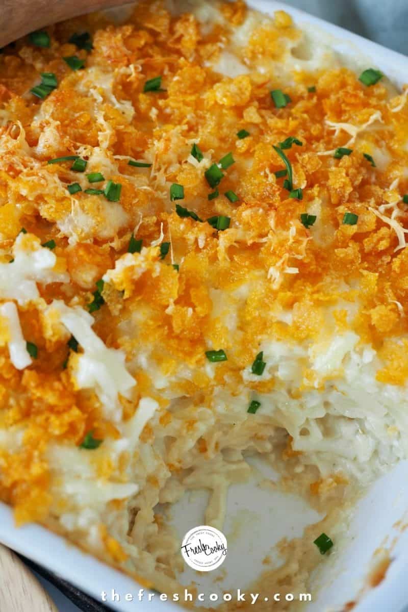 Close up of Cheesy Funeral Potatoes in white casserole dish, with a portion pulled out.