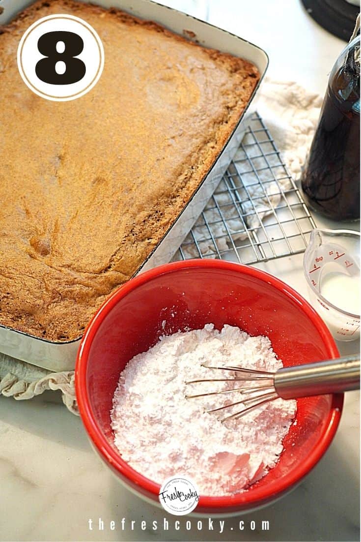 Mixing bowl with whisk with powdered sugar, vanilla and maple syrup and pumpkin cake baked in background