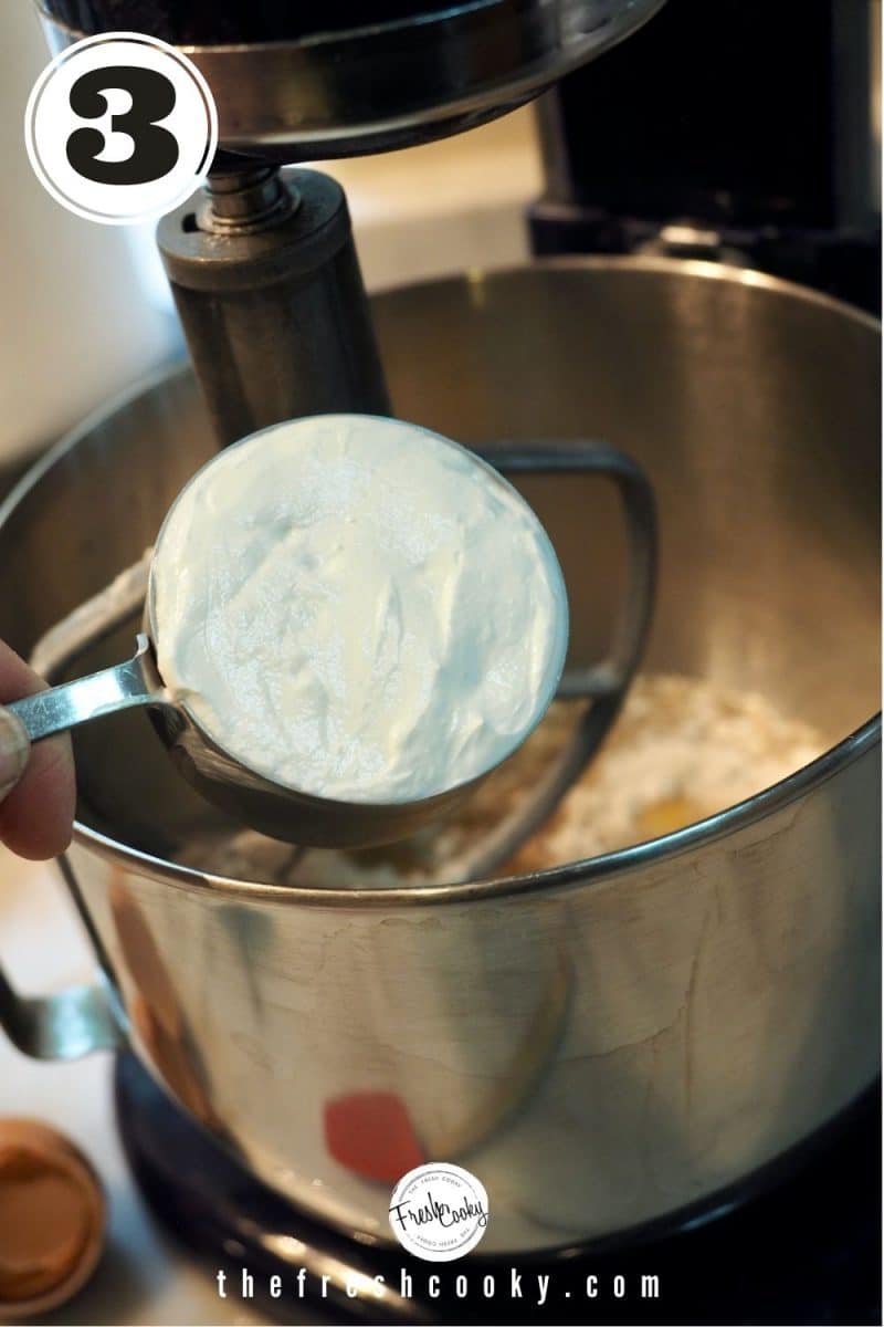 ½ cup measuring cup filled with Greek yogurt over stand mixing bowl