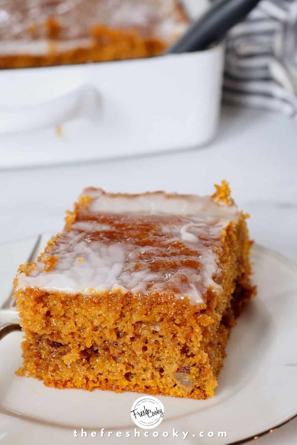 square slice of pumpkin spice cake on a white china plate, with baking pan in background.