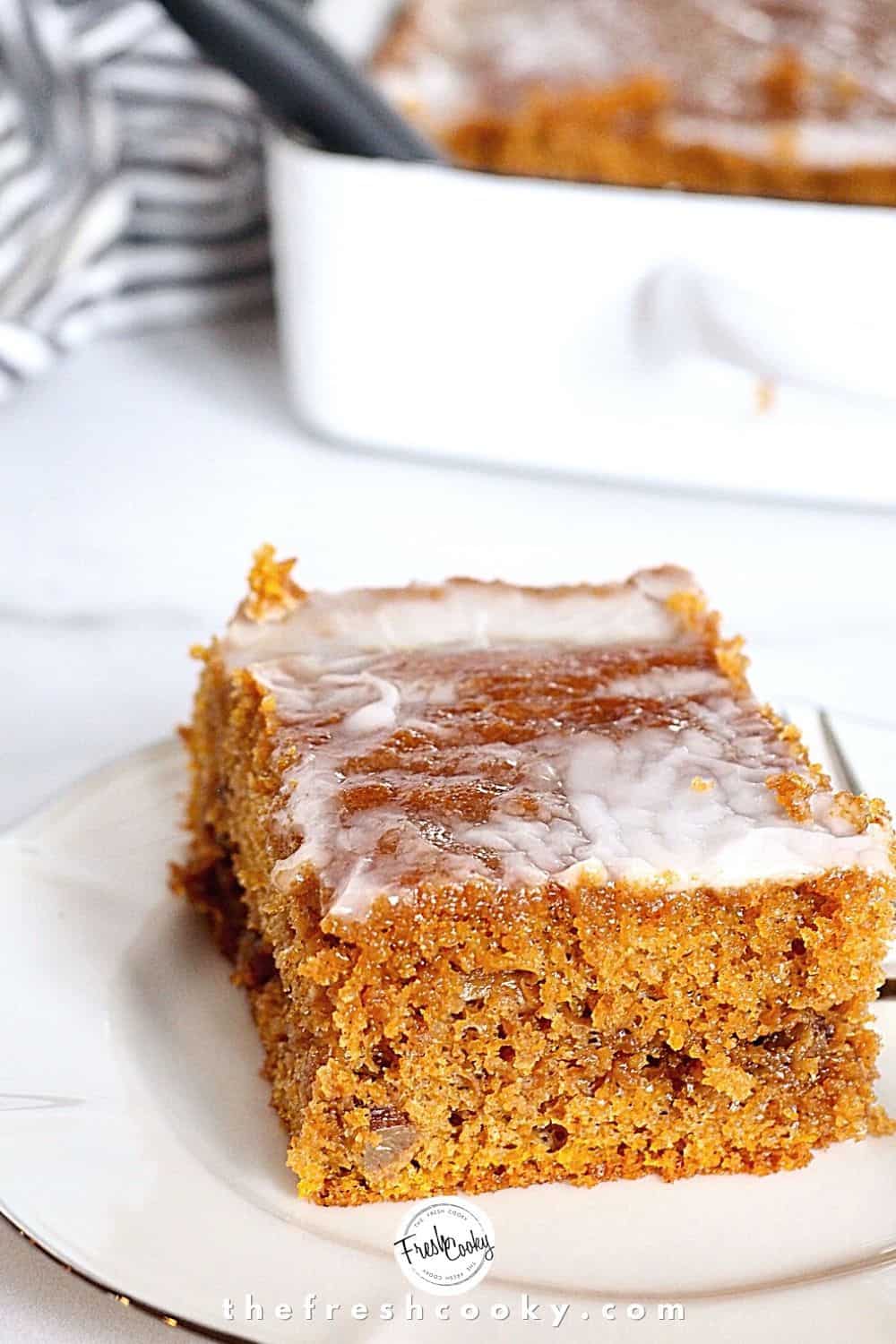 Pumpkin coffee cake slice on a plate with the whole spice cake behind.