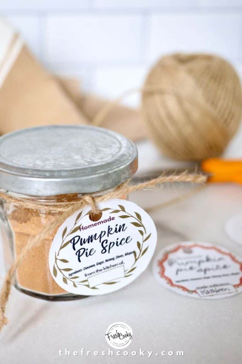 image of pumpkin pie spice mix in small jar with silver lid with cute gift tag and other gift tags on marble top with napkin, ball of string and scissors in background.
