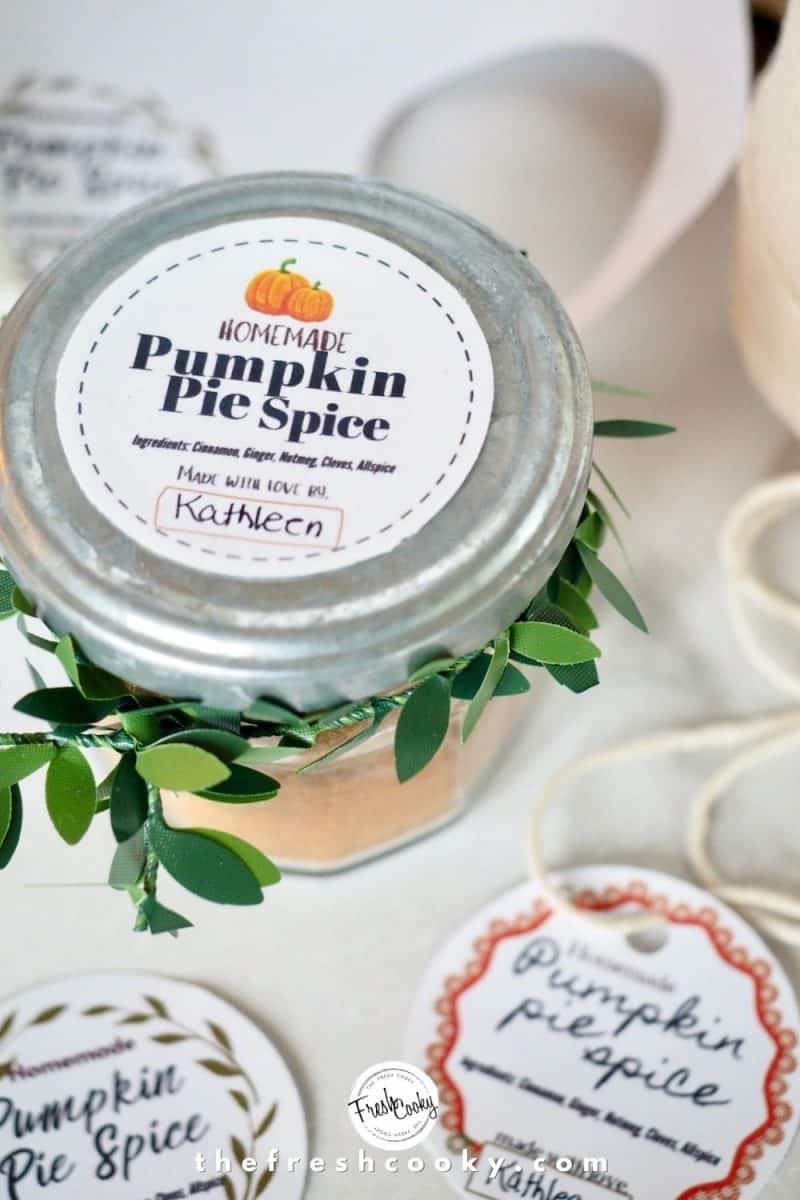 CLosed jar of pumpkin pie spice with silver lid, greenery tied on an pumpkin label on top
