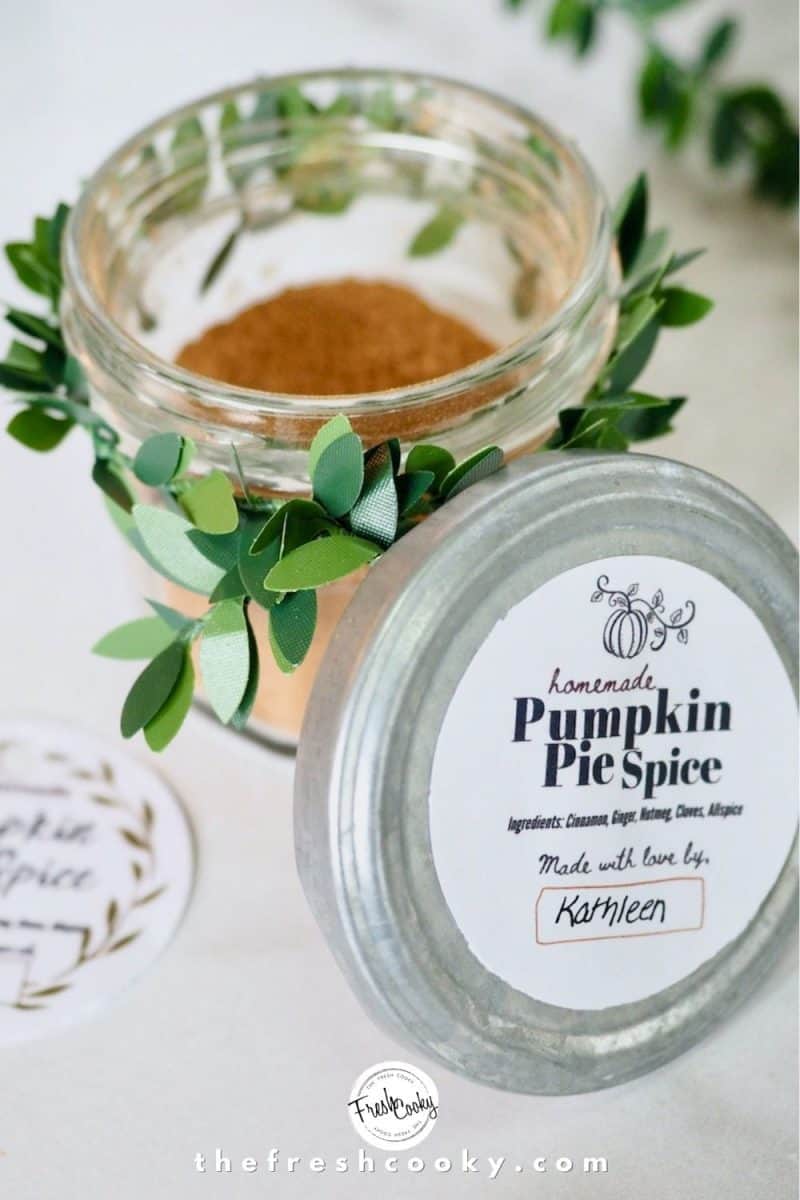 glass jar with pumpkin spice mixture inside, tied with greenery wired decor, lid leading against side with pumpkin spice label on top (free).