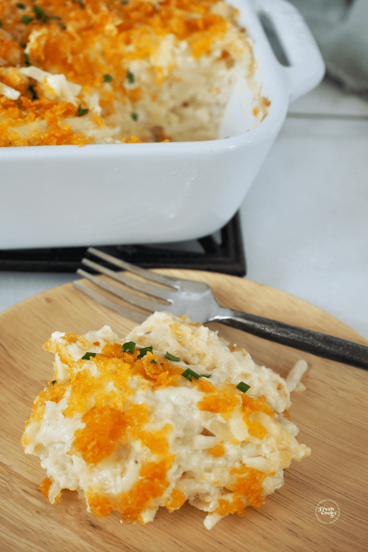 Serving of cheesy funeral potatoes on a plate with fork.