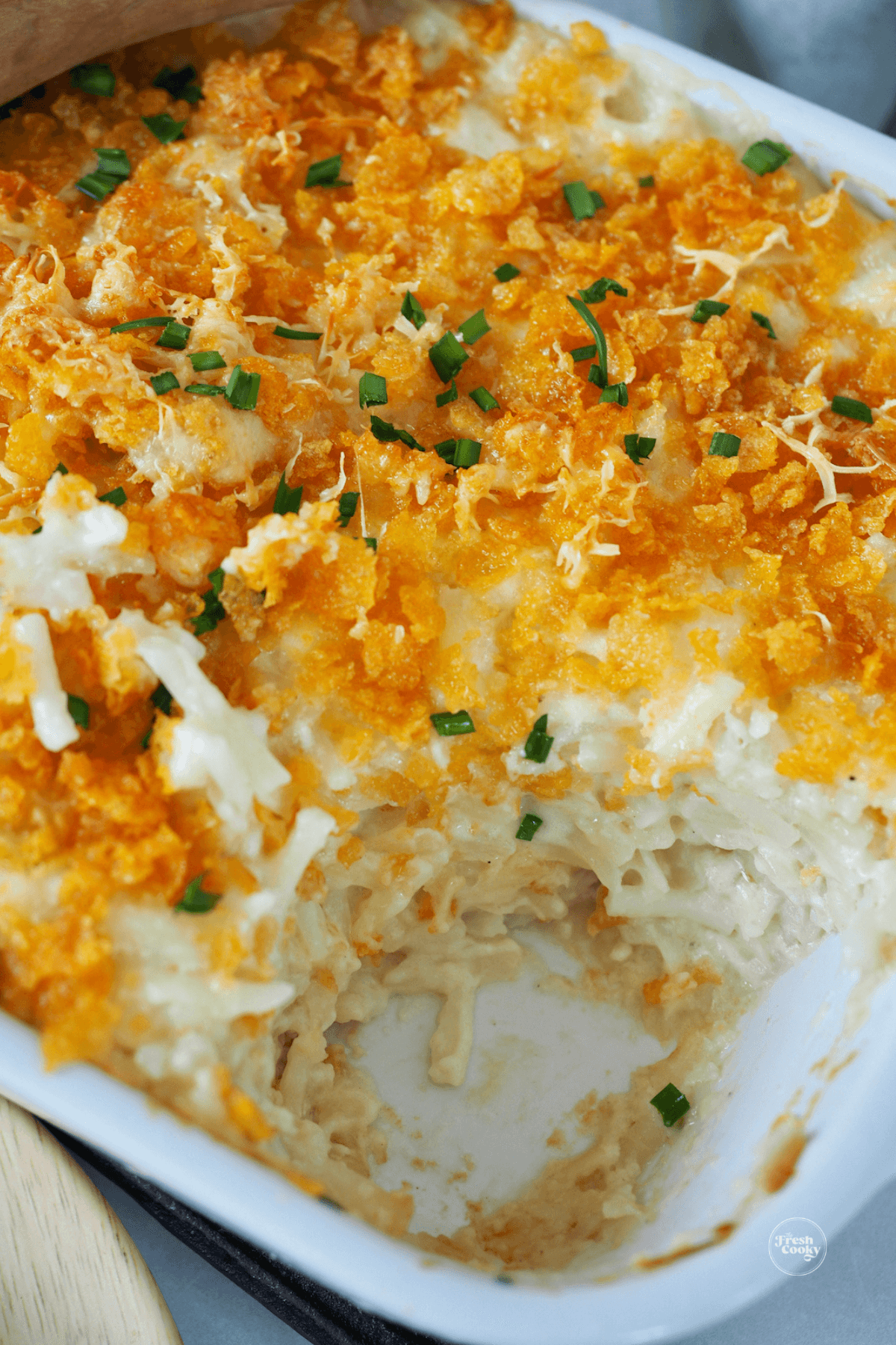 Hashbrown casserole in dish with serving removed, topped with corn flake topping.