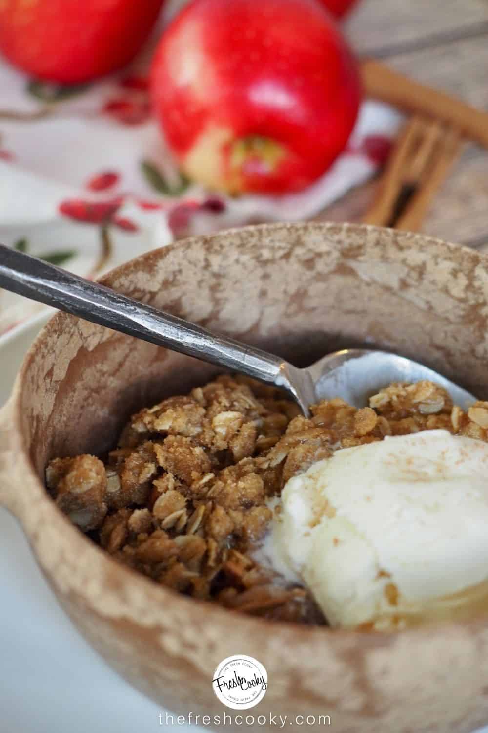 bowl filled with apple crisp and a scoop of vanilla ice cream with apples in background.