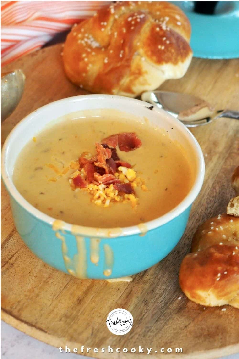 Large turquoise soup bowl filled with Beer Cheese Soup with soft pretzels on wooden charger surrounding the soup.