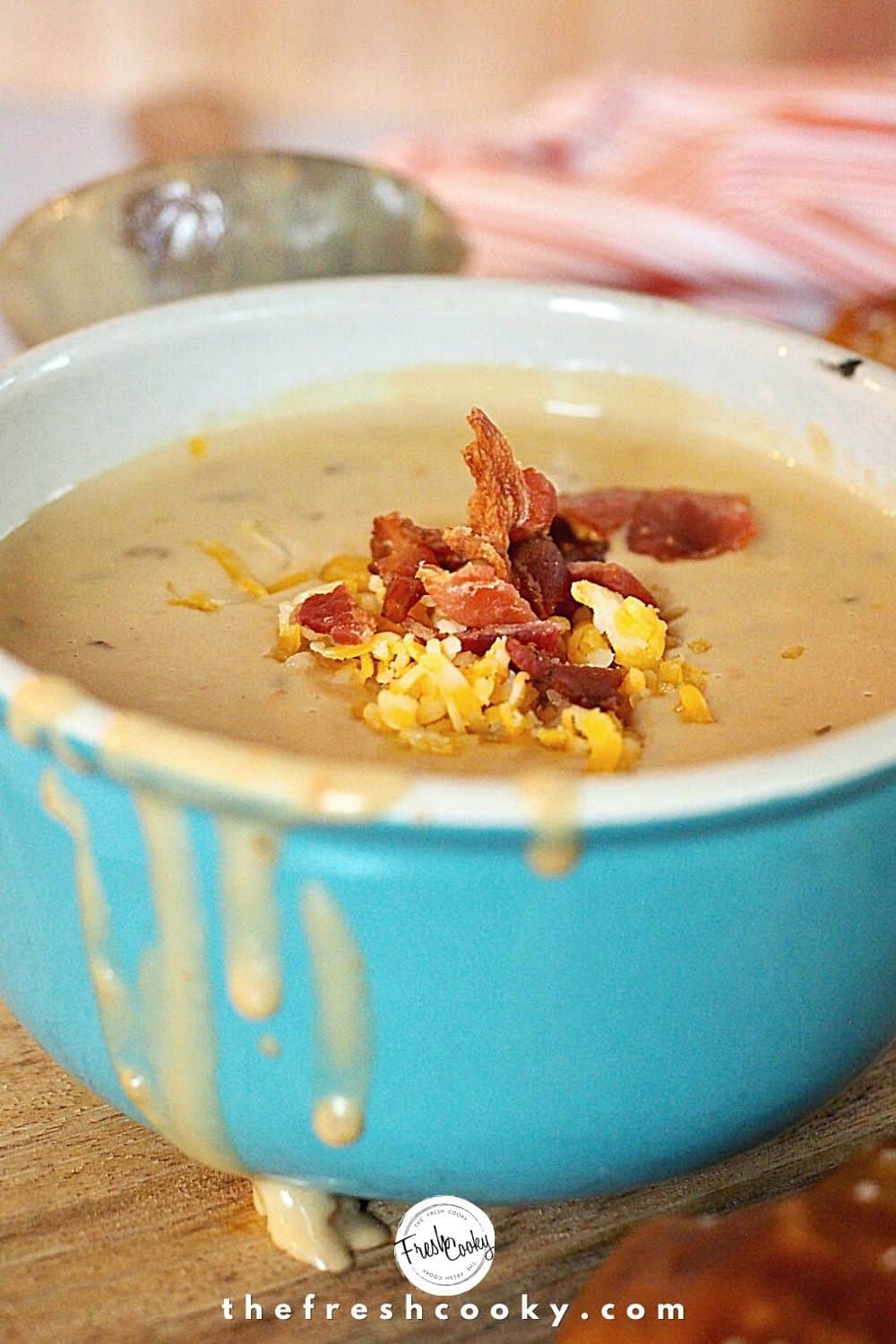 Close up shot of a turquoise bowl of beer cheese soup with shredded cheese and crumbled bacon on top.