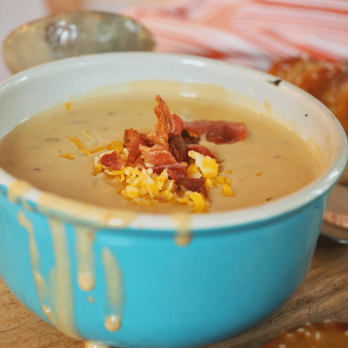 Beer and Cheese soup in turquoise bowl with bacon and cheese, square image.