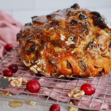 Loaf of cranberry walnut no knead bread on cooling rack with fresh cranberries and walnuts.
