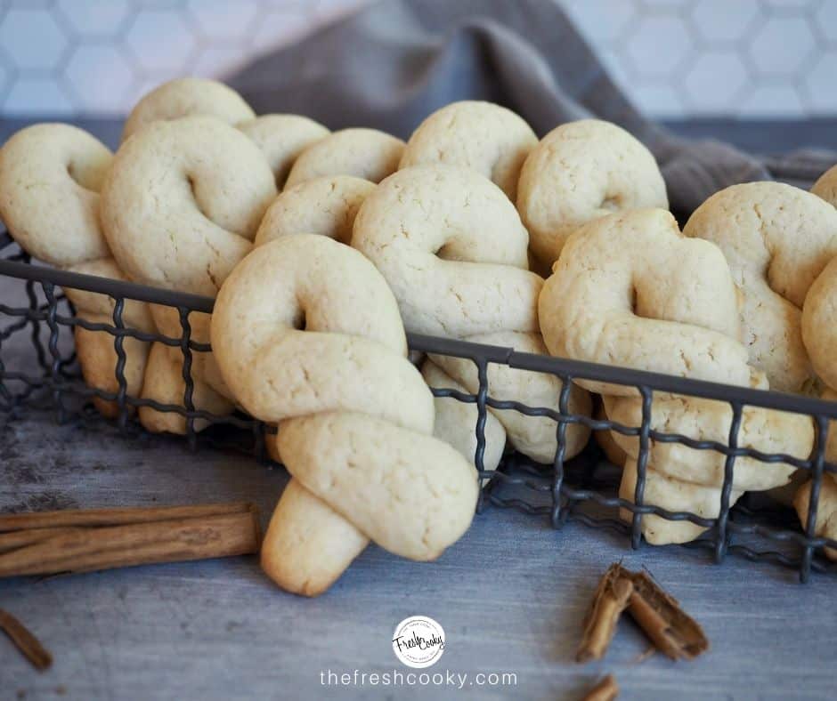 Facebook image for Koulourakia Greek Butter Cookies with them sitting in wire basket, smashed cinnamon sticks and a dark blue napkin