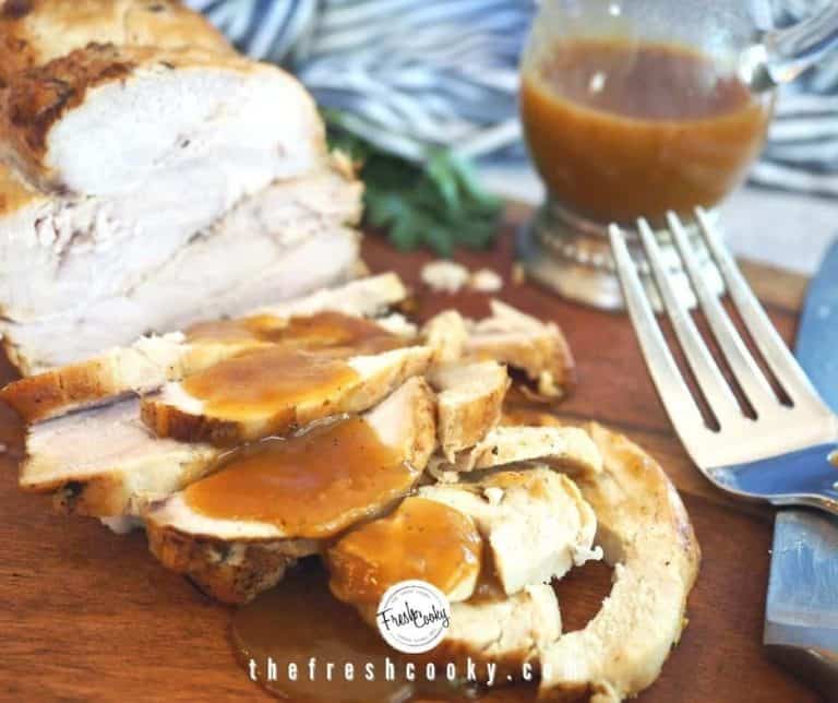 Facebook image of Sliced Turkey Breast on cutting board with pan gravy drizzled on top. Large fork in foreground with pitcher of gravy behind.