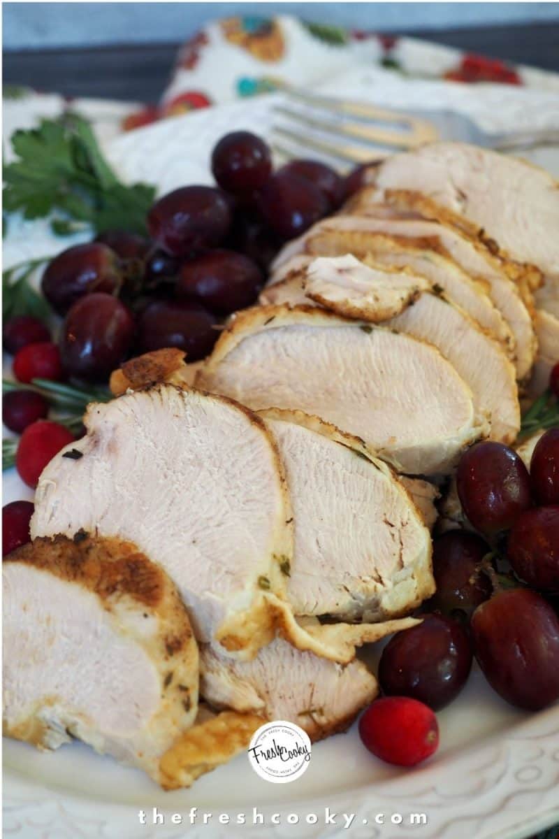 Instant Pot Turkey Breast image with partially sliced turkey breast on platter with cranberries, grapes and fresh herbs surrounding the turkey.