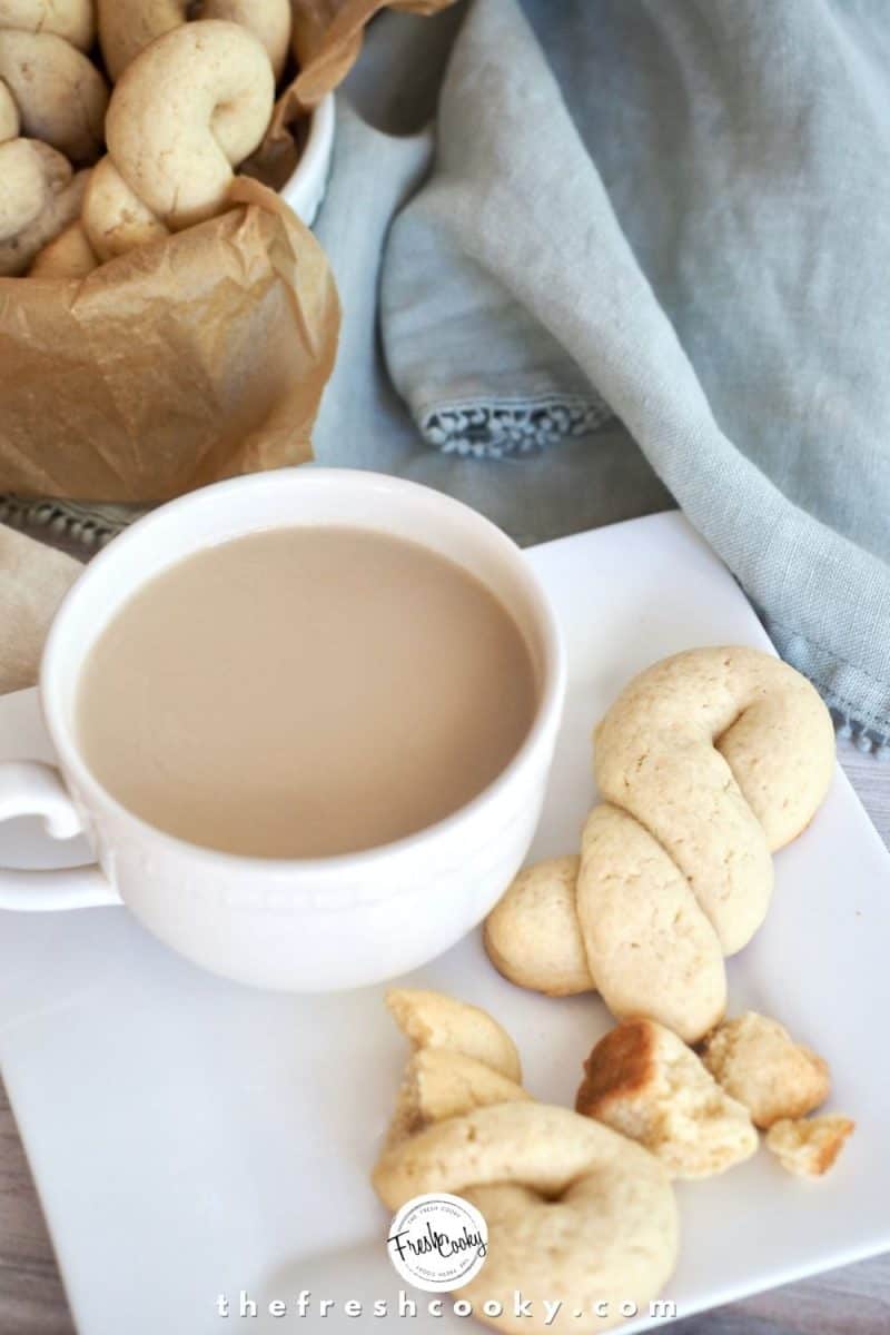 Greek Butter Cookie twists in a square white plate with a cup of tea and additional cookies in background