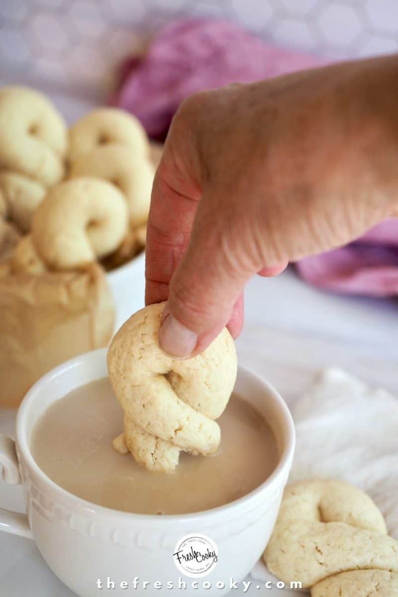 Hand dunking Greek Butter Cookie into cup of black tea with cream