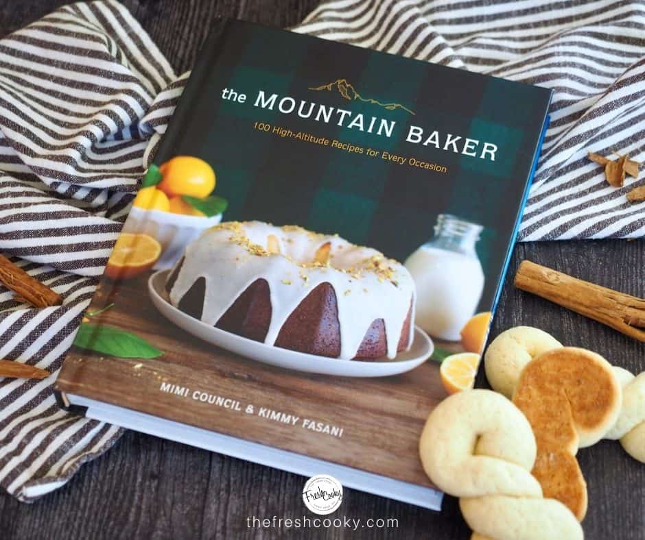 Image of the Mountain Baker Cookbook with homemade Koulourakia Greek Butter Cookies sitting near, cinnamon sticks and a striped tea towel