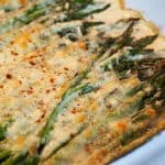 corner shot of cheesy baked asparagus with melted cheese in a casserole dish