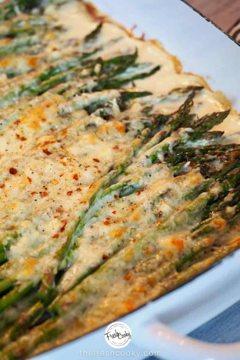 corner shot of cheesy baked asparagus with melted cheese in a casserole dish