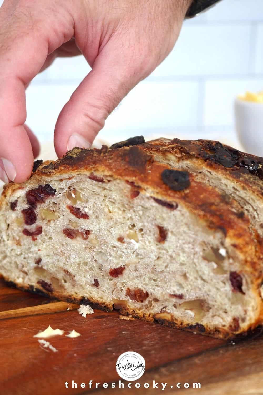 Man's hand pulling a freshly sliced piece of cranberry walnut bread from loaf.