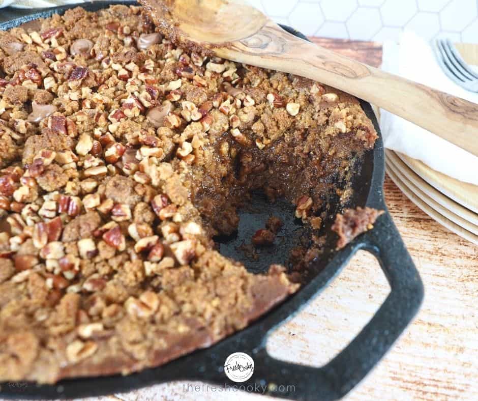 Chocolate Pumpkin Graham Crisp in cast iron skillet with scoop spooned out and wooden spoon leaning on top.