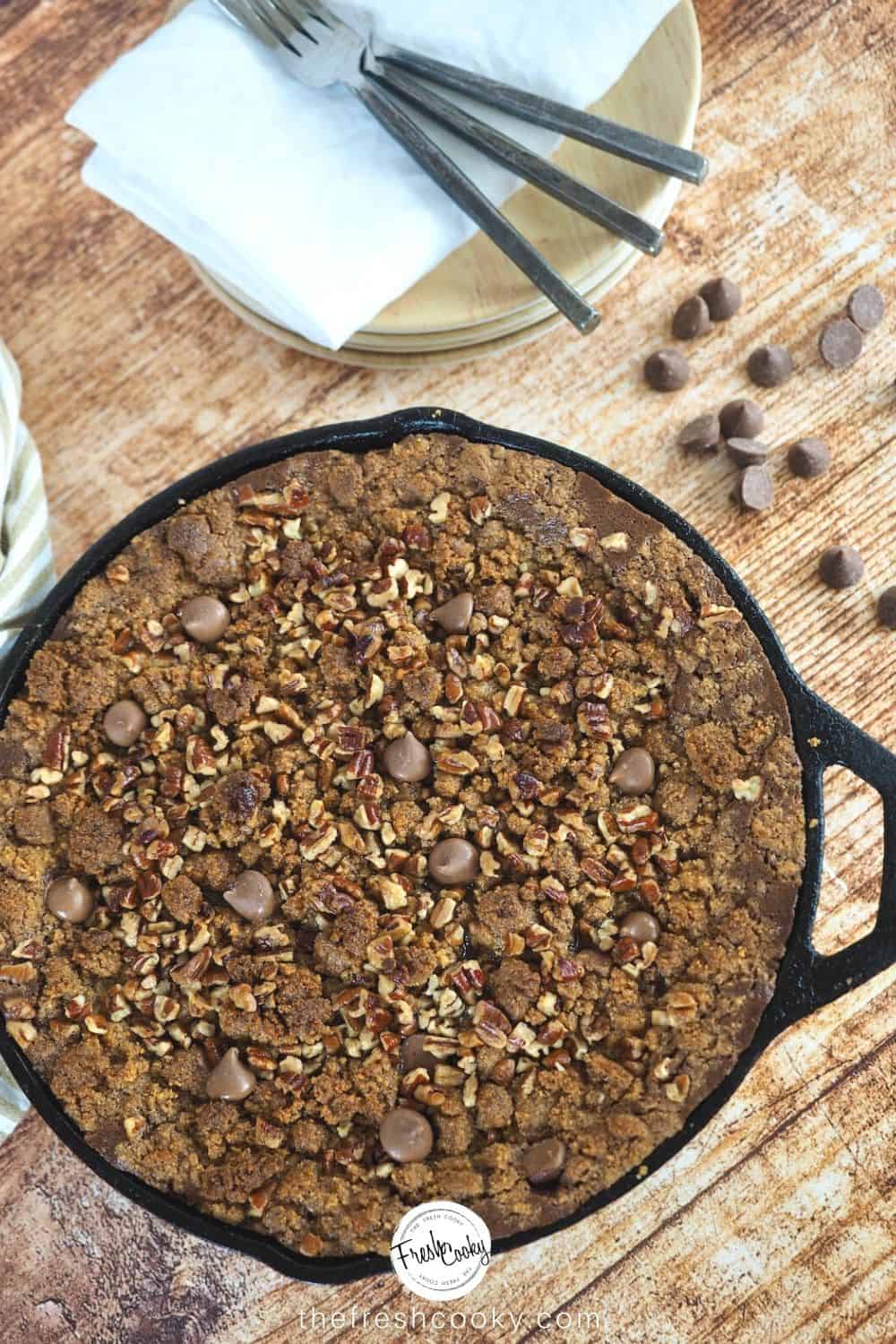 Image of cast iron skillet with chocolate pumpkin crisp, chocolate chips and forks and napkins laying behind.