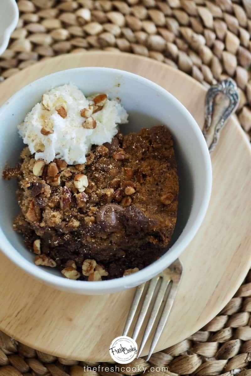 Scoop of chocolate crisp in white bowl with fresh whipped cream on top, sprinkled with chopped pecans.